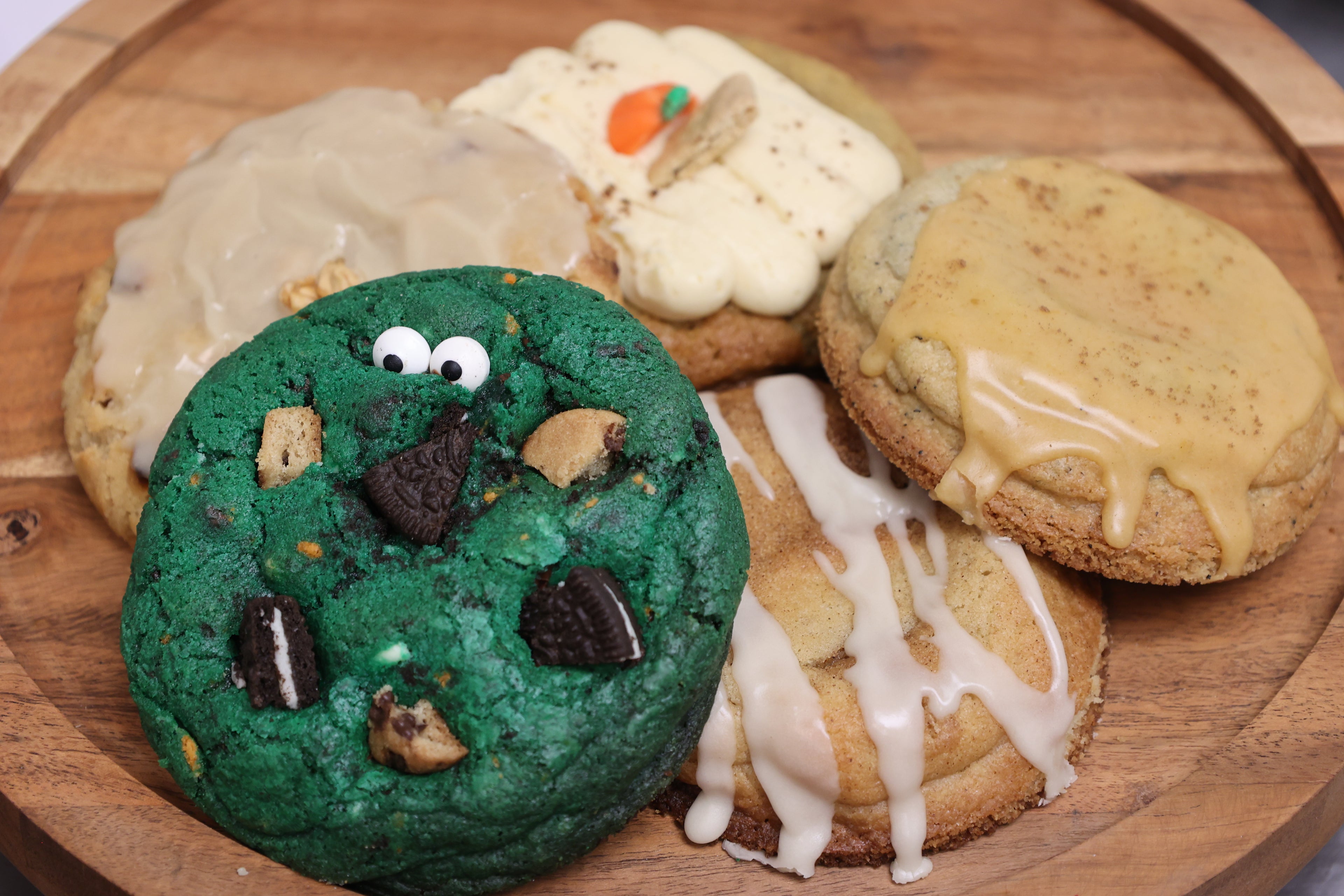 Fall assorted cookies including a green cookie with face decorations on a wooden plate.