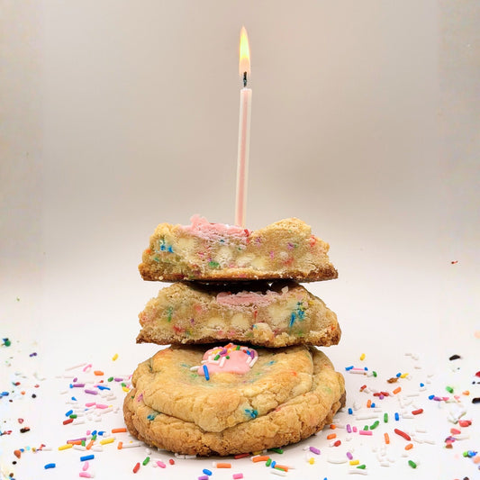 Stack of cookies with a lit candle on top, surrounded by colorful sprinkles against a plain background