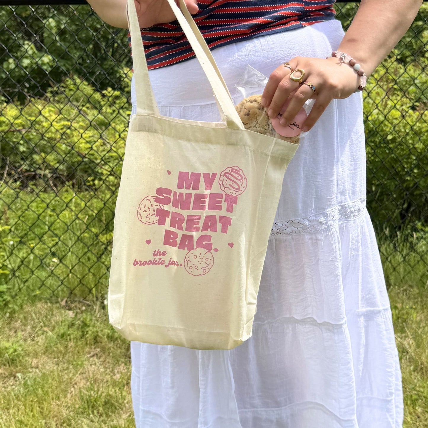 Person holding a beige tote bag with pink text in an outdoor setting.
