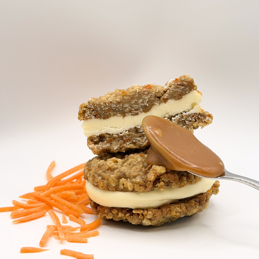 Two layered cookie sandwich with cream and caramel, topped with a spoonful of caramel, on a white background.